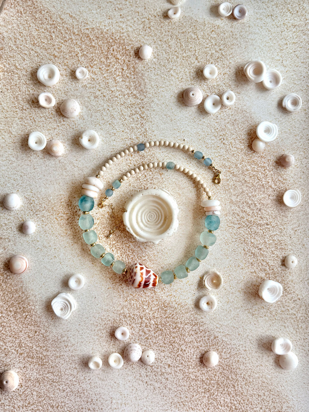 necklace arranged in a circle on a sandy surface, surrounded by scattered seashells.