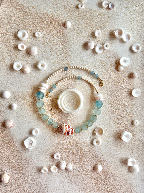 necklace arranged in a circle on a sandy surface, surrounded by scattered seashells.